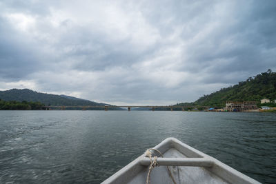 Cropped image of boat in lake against cloudy sky