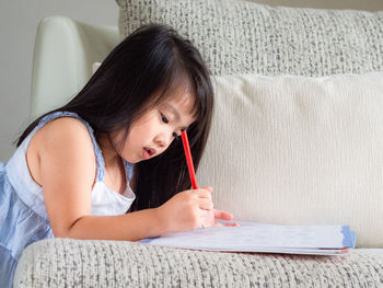 Girl writing in book on sofa at home