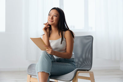Young woman holding notebook sitting on chair