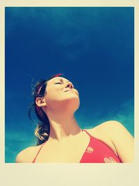 Low angle view of young woman against blue sky