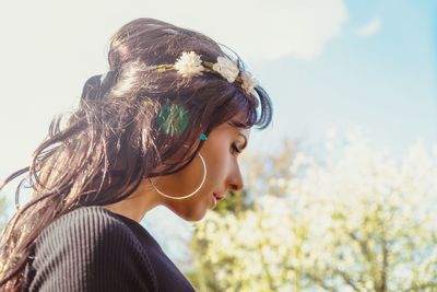 Woman wearing flowers while looking away against trees and sky