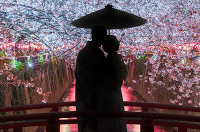 A couple sweetens in the dark on a bridge during cherry blossom season in tokyo 