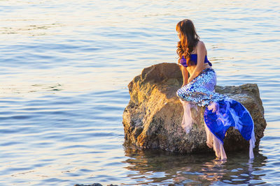 Woman sitting on rock in sea