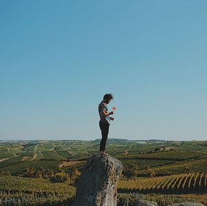 Man holding drink while standing on rock at field against clear sky