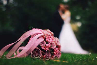 Pink rose bouquet against wedding couple on field