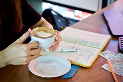 Close-up of woman holding coffee cup on table