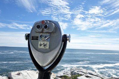 Close-up of coin-operated binoculars by sea against sky