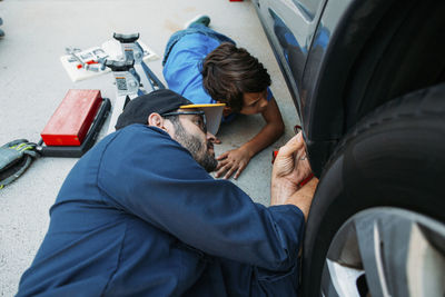 High angle view of serious father teaching son to repair car at driveway