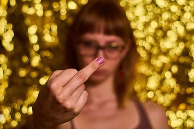 Close-up of young woman showing obscene gesture against defocused lights at night