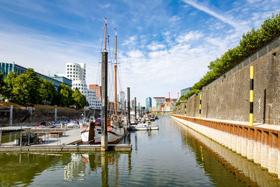 Sailboats moored on canal amidst buildings in city against sky