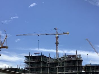 Low angle view of crane at construction site against sky