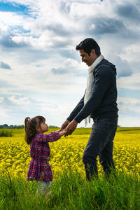 Side view of mother and daughter standing on field against sky