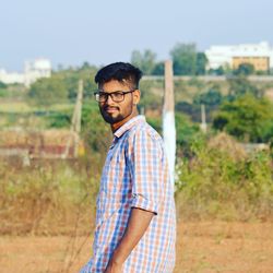 Portrait of young man standing on field against clear sky