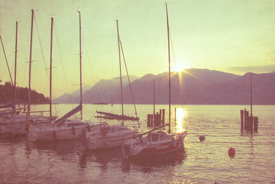 Boats moored in lake by mountain during sunset