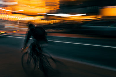 Blurred motion of person riding bicycle on road at night