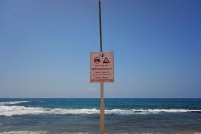 Information sign on beach against clear sky