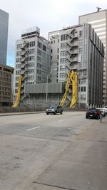 Cars on road by buildings in city against sky