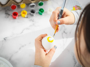Little caucasian girl paints an easter egg with a brush with yellow acrylic pain