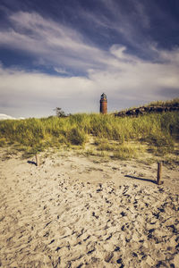 Lighthouse on sand by sea against sky