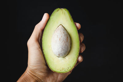 Close-up of hand holding apple against black background