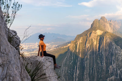 Man sitting on rock looking at mountains against sky