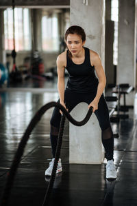 Confident young woman exercising with ropes in gym