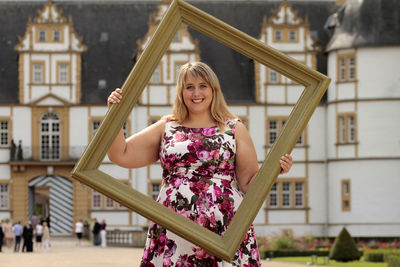 Portrait of happy fashion model holding picture frame on street