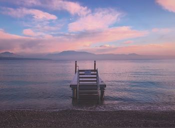 Empty chair on beach against sky during sunset