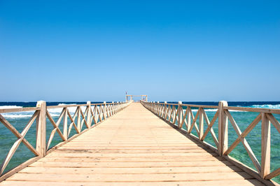 Footbridge over sea against clear blue sky