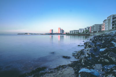 Buildings by sea against clear blue sky