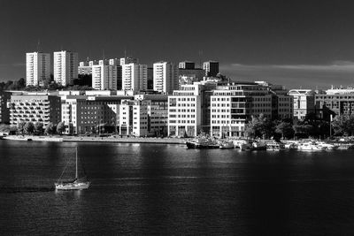 Sailboats in sea by modern buildings against sky in city