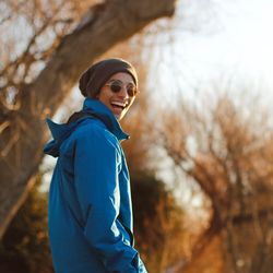 Man in sunglasses laughing while standing against tree at forest