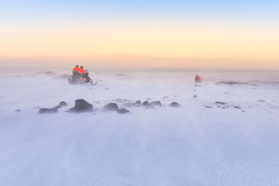 People on snow covered land against sky during sunset