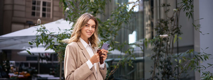 Portrait of young woman standing against buildings