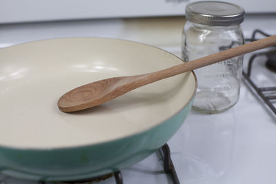 Close up of a clean frying pan with a wooden spoon in it and an empty glass jar next to it