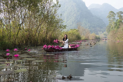 Woman with flowers by lake against trees