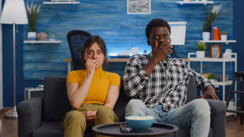Portrait of couple eating popcorn sitting on sofa at home