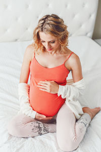 Smiling pregnant woman sitting on bed at home