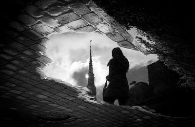 Reflection of silhouette woman and church on puddle