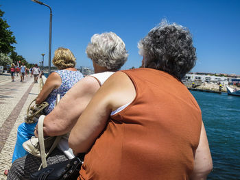 Rear view of people sitting by sea against sky