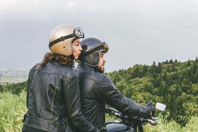 Rear view of couple looking away while sitting on motorcycle against sky