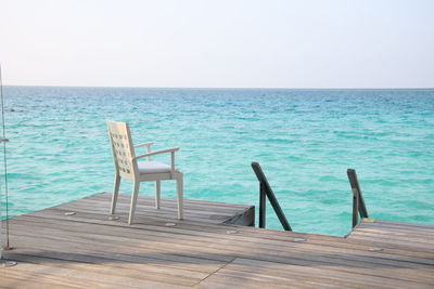 Empty chairs by swimming pool against sky