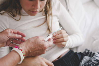 Cropped image of grandmother showing thermometer to granddaughter at bedroom