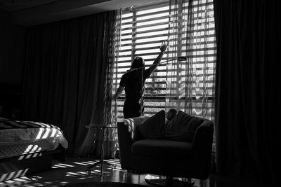 Rear view of man standing by window on sofa at home