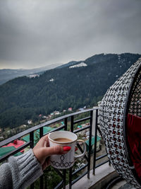 Person with coffee and mountains against sky