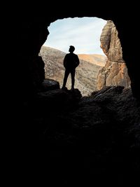 Silhouette man standing on rock against sky