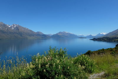 Scenic view of lake and mountains against clear blue sky