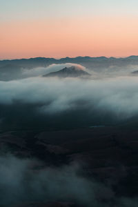 Scenic view of mountains shrouded in clouds against sky during sunset