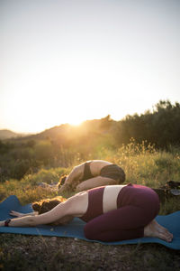 Women practicing yoga on mats against clear sky at sunset