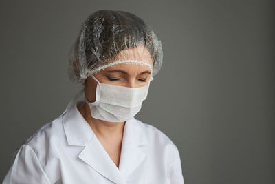 Close-up of female doctor wearing mask with eyes closed against gray background